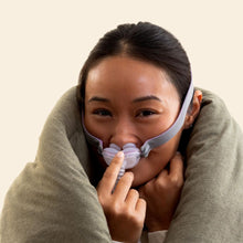 Load image into Gallery viewer, A woman wrapped in a thick gray blanket is wearing a nasal CPAP mask with a light purple cushion and tube, set against a plain light beige background.
