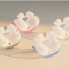 Load image into Gallery viewer, Four translucent silicone earplugs in different sizes (XS, S, M, L) with pink, beige, white, and blue accents, arranged on a beige surface with a gray background.
